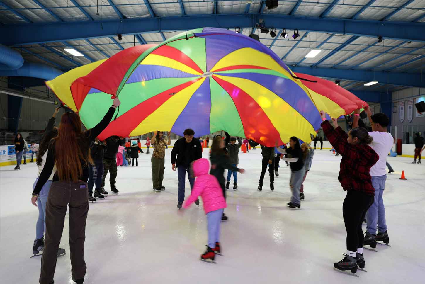Children and adults playing a game of parachute on the ice during a public skating open skate session at the Ice Factory