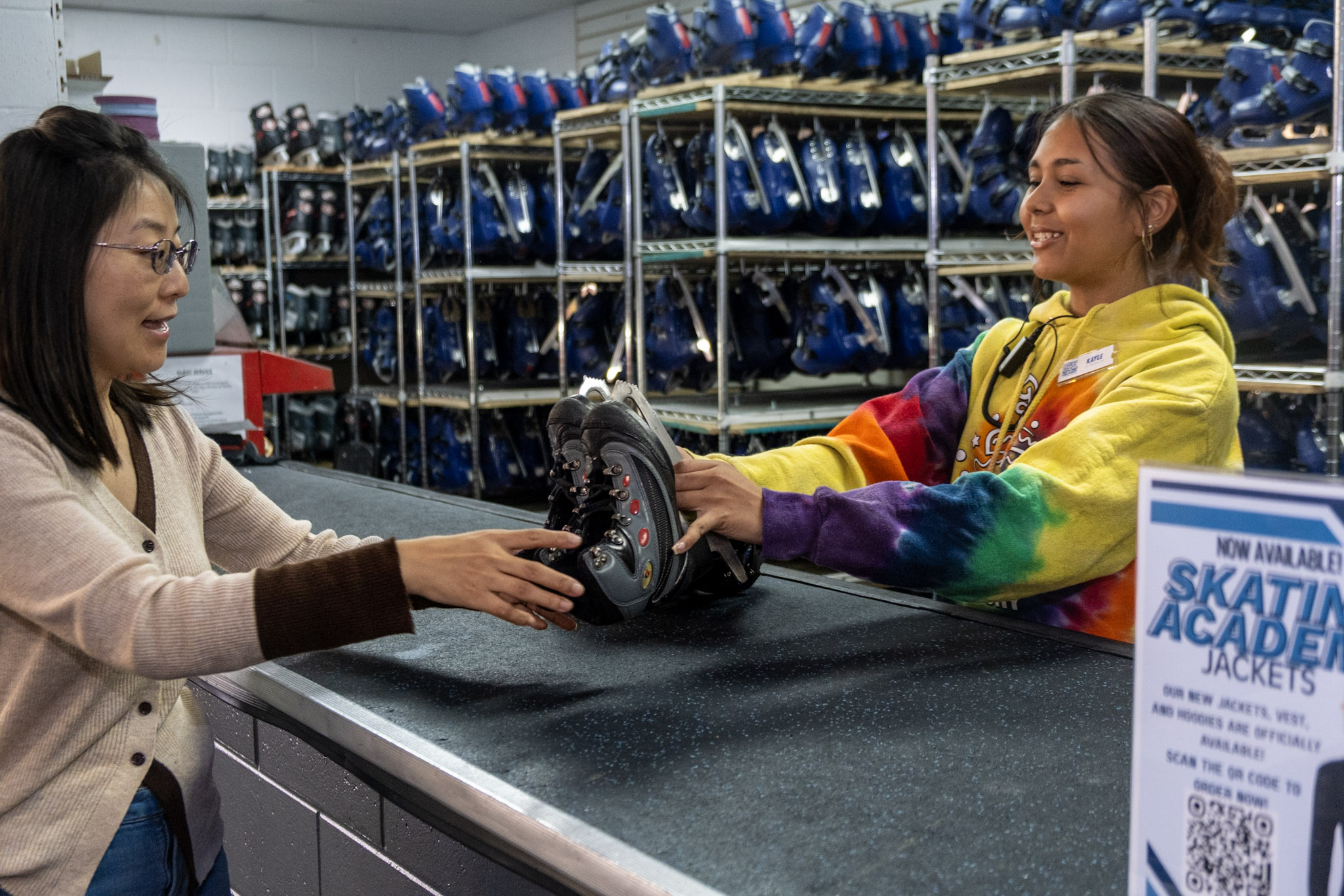 a friendly employee handing out a pair of rental ice skates for a public skating session at the Ice Factory
