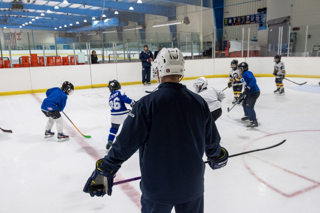 Youth hockey practice session at Ice Factory, featuring a coach observing players on the ice, focusing on skill development and teamwork.